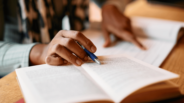 Open book on table with a person's hand gliding over the text
